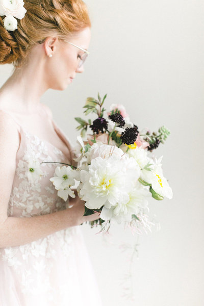 A bride in a white lace dress holding a bouquet of white flowers and greenery.