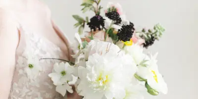 A bride in a white lace dress holding a bouquet of white flowers and greenery.