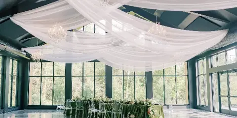 A wide shot of a wedding venue featuring elaborate white ceiling draping, hanging crystal chandeliers, and a decorated head table.