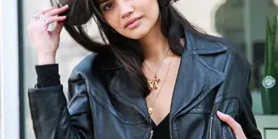 A professional fashion portrait of a woman wearing a black leather jacket and gold jewelry, posing outdoors.