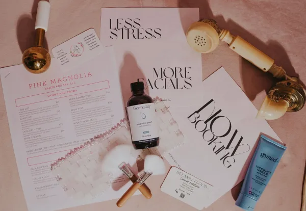 A flat-lay photograph of a beauty salon service menu, business card, makeup brushes, and skincare products.