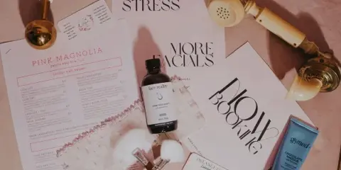 A flat-lay photograph of a beauty salon service menu, business card, makeup brushes, and skincare products.