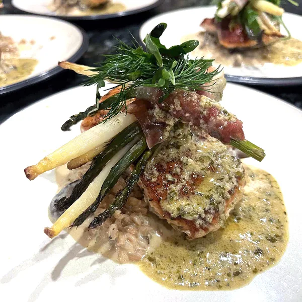 A close-up of a plated gourmet dish featuring a seared protein, asparagus, and a creamy sauce.