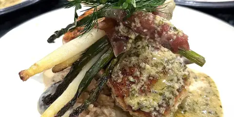 A close-up of a plated gourmet dish featuring a seared protein, asparagus, and a creamy sauce.