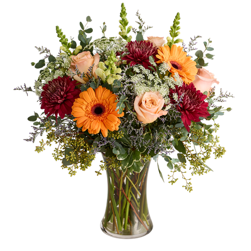 A floral arrangement featuring orange gerbera daisies, peach roses, and red dahlias in a clear glass vase.