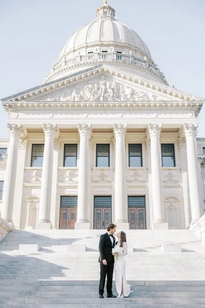 A bride and groom standing on the steps of a large, white domed building.