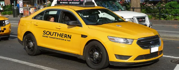 Yellow taxi sedan with 'Southern Maine Transportation & Taxi' branding driving on a city street