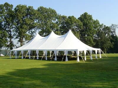 A large white event tent set up on a grassy lawn with trees in the background.
