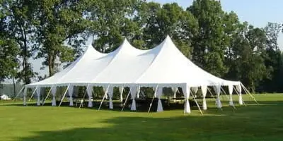 A large white event tent set up on a grassy lawn with trees in the background.