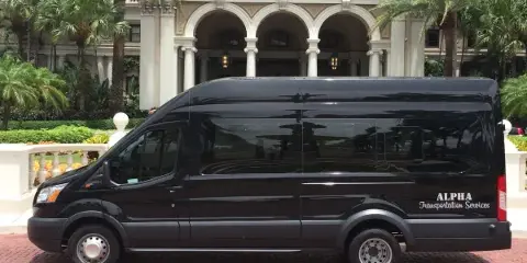 A black Alpha Transportation Services Sprinter van parked on a brick driveway in front of a luxury hotel or venue.