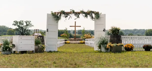 Outdoor wedding ceremony setup with a floral arch, white chairs, and decorative furniture.