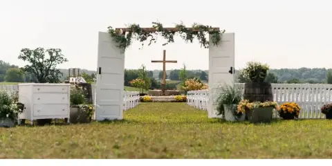 Outdoor wedding ceremony setup with a floral arch, white chairs, and decorative furniture.