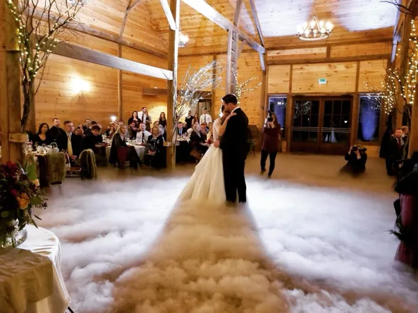 A bride and groom dancing on a fog-covered dance floor at a wedding reception in a wooden hall.