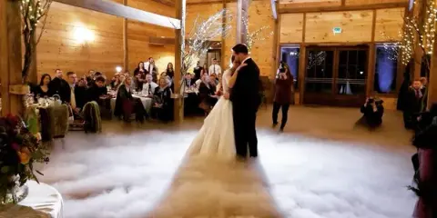 A bride and groom dancing on a fog-covered dance floor at a wedding reception in a wooden hall.