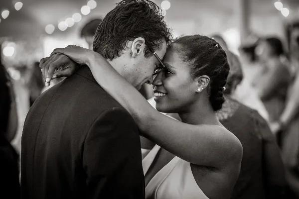 A black and white photograph of a bride and groom dancing closely together at a wedding reception.