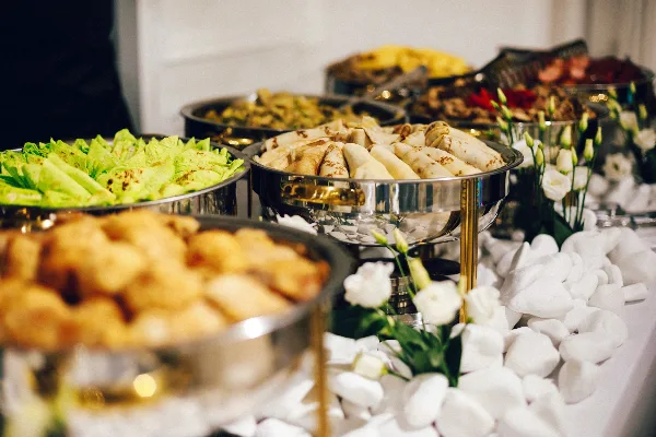 A catering buffet featuring chafing dishes with food and white flowers on a table.