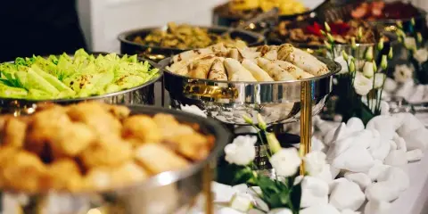 A catering buffet featuring chafing dishes with food and white flowers on a table.