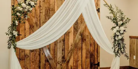 A wedding arch decorated with white flowers and greenery in front of a brick wall.