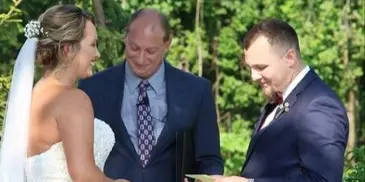 A bride and groom exchanging vows outdoors with an officiant standing between them.