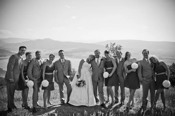 A black and white photograph of a wedding party posing outdoors with a mountain landscape in the background.