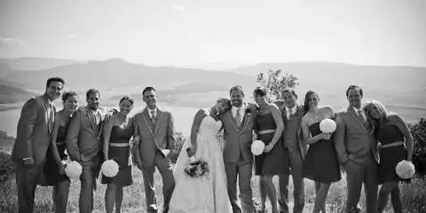 A black and white photograph of a wedding party posing outdoors with a mountain landscape in the background.