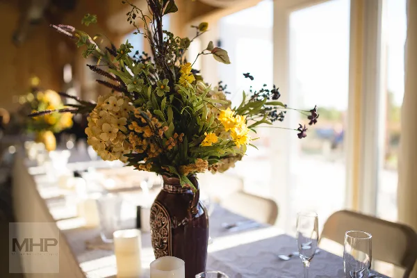 A professionally styled event table with a large floral arrangement in a ceramic vase, glassware, and table setting.