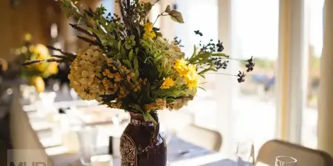 A professionally styled event table with a large floral arrangement in a ceramic vase, glassware, and table setting.