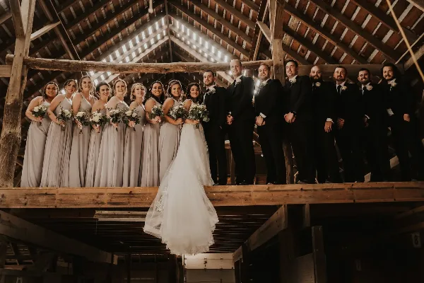Wedding party posing on a wooden loft inside a rustic barn venue with exposed beams and skylight.