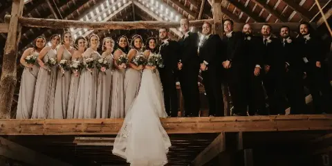 Wedding party posing on a wooden loft inside a rustic barn venue with exposed beams and skylight.