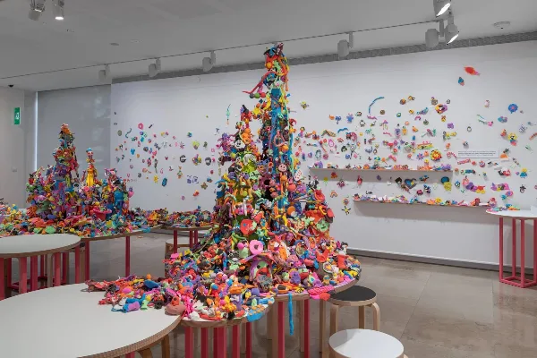 A colorful, large-scale art installation featuring towers of small figures and objects in a museum gallery.