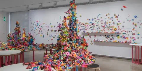 A colorful, large-scale art installation featuring towers of small figures and objects in a museum gallery.