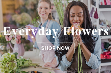 A florist arranging fresh flowers in a shop setting with another person in the background.