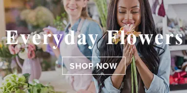 A florist arranging fresh flowers in a shop setting with another person in the background.