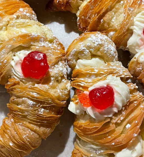 Close-up of a flaky pastry topped with whipped cream and a red cherry.