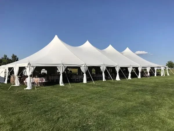 Large white event tent set up on a grassy lawn with tables and chairs visible inside under a clear blue sky.