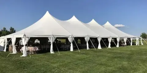 Large white event tent set up on a grassy lawn with tables and chairs visible inside under a clear blue sky.