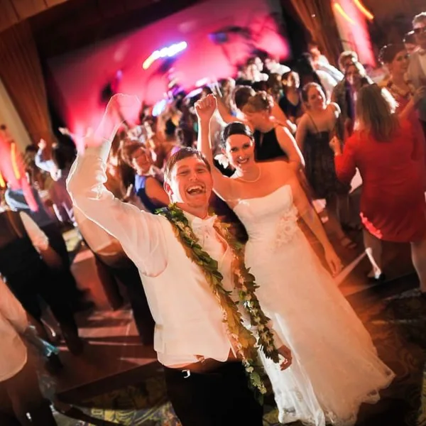 A bride and groom dancing at a wedding reception with a crowd of guests in the background.