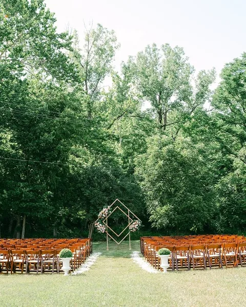 Outdoor wedding ceremony setup with rows of wooden chairs, a floral arch, and a tree-lined backdrop at a scenic venue.