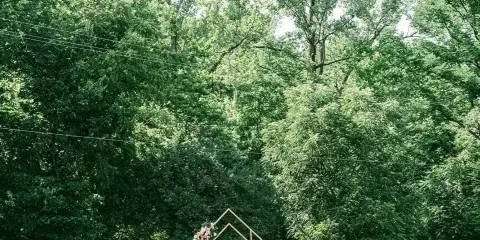 Outdoor wedding ceremony setup with rows of wooden chairs, a floral arch, and a tree-lined backdrop at a scenic venue.