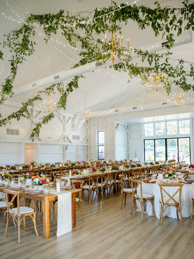 Interior of a wedding venue featuring a large floral and lighting installation on the ceiling above a banquet hall.