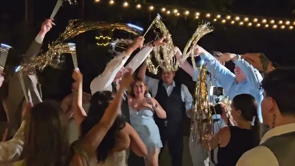 A DJ and MC at a wedding reception holding a microphone while guests celebrate with sparklers.