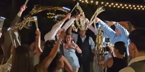A DJ and MC at a wedding reception holding a microphone while guests celebrate with sparklers.