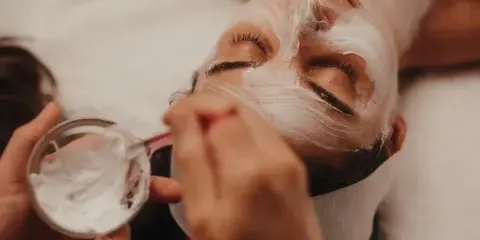 Aesthetician applying a white facial mask to a client's face during a spa treatment.