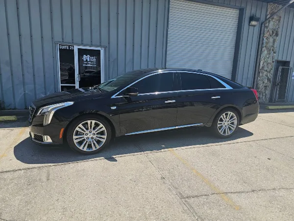 A black luxury sedan parked in front of a commercial building with a His & Hers Limousines sign on the door.