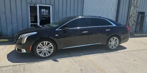 A black luxury sedan parked in front of a commercial building with a His & Hers Limousines sign on the door.
