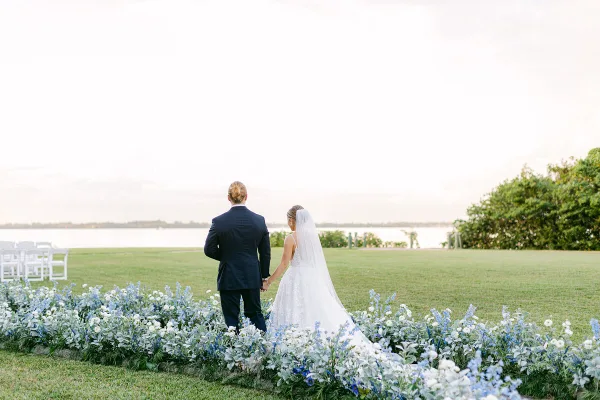 A bride and groom standing together at an outdoor wedding venue with floral decorations and white chairs.