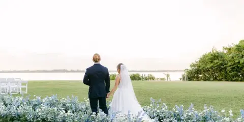 A bride and groom standing together at an outdoor wedding venue with floral decorations and white chairs.