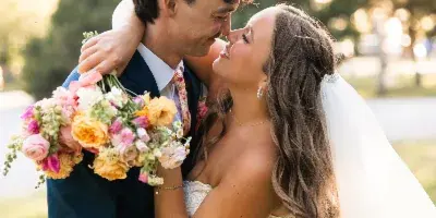 A bride and groom embracing and smiling at each other outdoors, with the bride holding a colorful bouquet.
