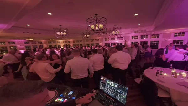 A DJ mixing music at a wedding reception with a large crowd dancing in the background.