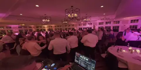 A DJ mixing music at a wedding reception with a large crowd dancing in the background.
